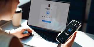 Over the shoulder view of young woman logging in online account with Two-Factor Authentication (2FA) security system visa smart phone and laptop.