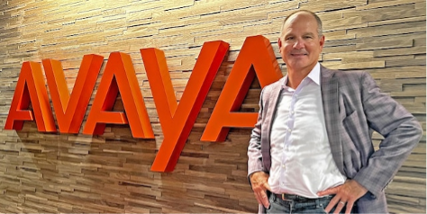 Avaya CEO Alan Masarek stood in front of red Avaya logo.