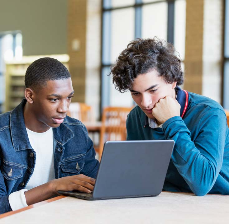 Two teenage boys in library using laptop