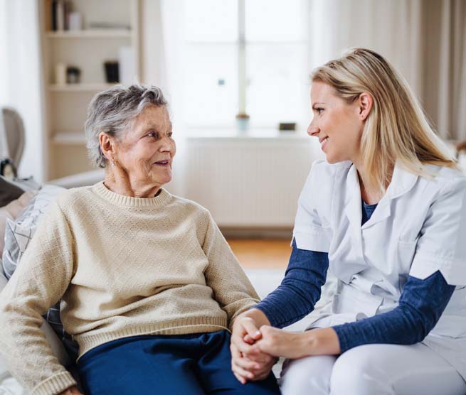 A nurse talking to a senior patient sitting on bed at home