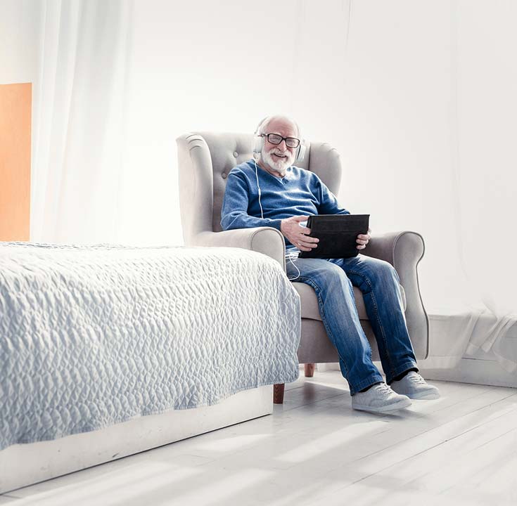 Elderly man sat in his room with laptop and headphones