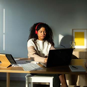 Woman with headphones on sitting at her computer desk looking at a laptop