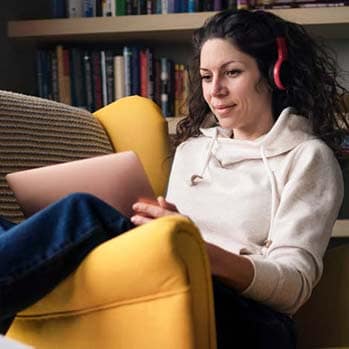 Woman with headphones on sitting on the couch looking at her laptop