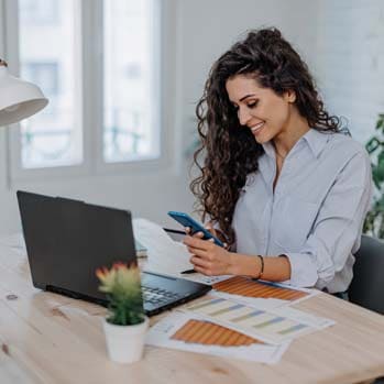 Woman is looking at her phone and holding her credit card.