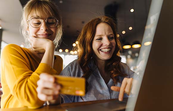 Two happy female friends with laptop and credit card in a cafe