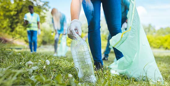 An unrecognizable woman holds a plastic garbage bottle that she puts in a recycling bag for cleaning. 