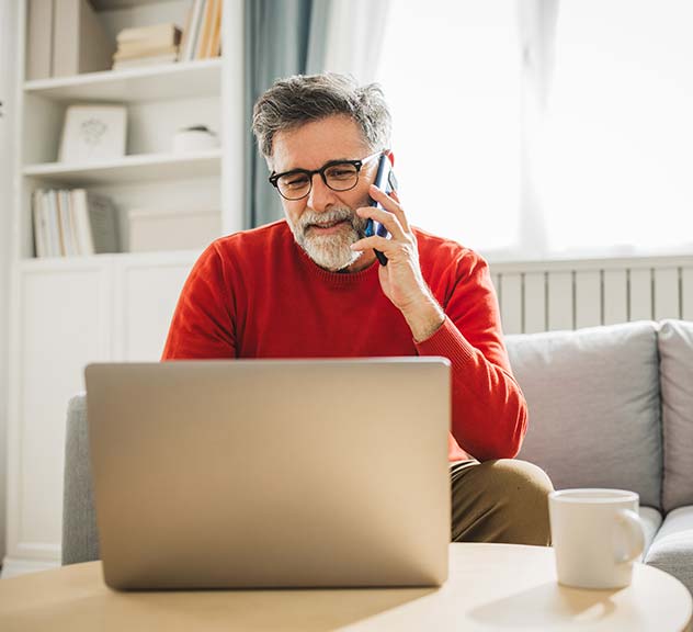 Man in his house talking on cellphone and working on laptop.