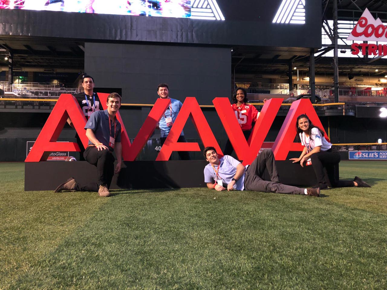 Avaya team members at a statue of large Avaya logo