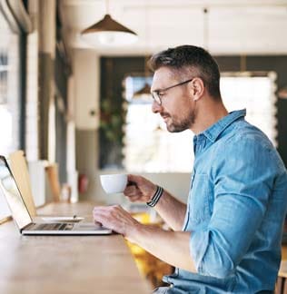 Man drinking coffee while working on his laptop