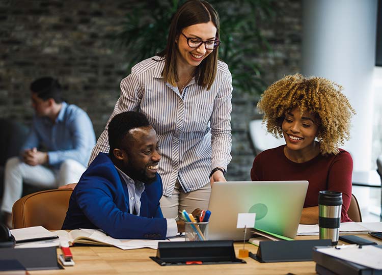 Three diverse young business colleagues smiling while reviewing something on laptop