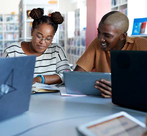 Two students holding digital tablet while studying in library