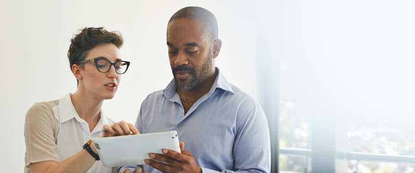 Coworkers standing in meeting room scrolling on digital tablet