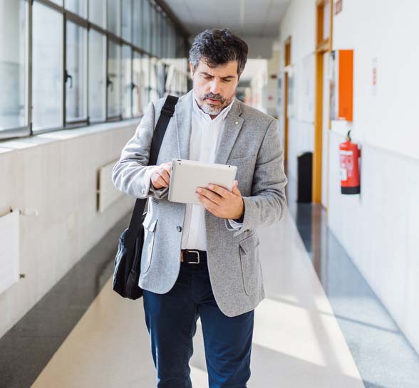 Professor using digital tablet while walking in corridor at university