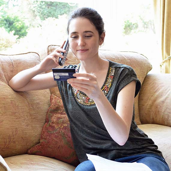 Woman holding up her credit card while talking on the phone with customer service.