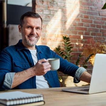 Smiling businessman with coffee cup sitting with laptop