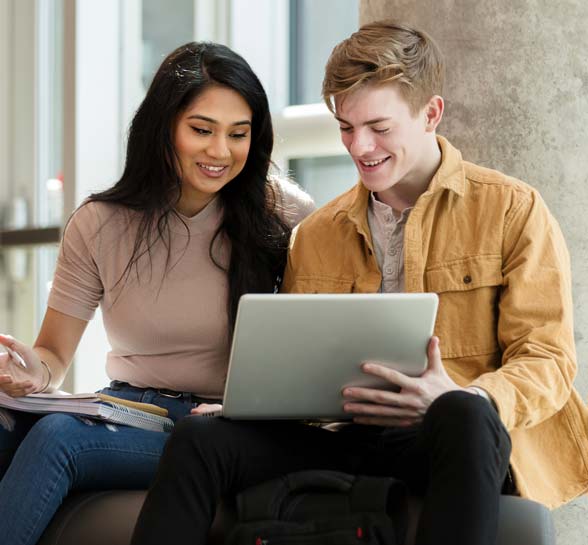 College couple smile while using a laptop to study before class.