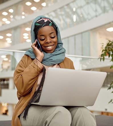 Woman with headscarf talking on the phone and looking at her laptop