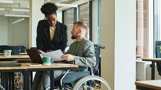 Businessman in wheelchair having discussion over document with colleague in office.