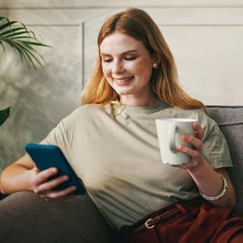 Woman drinking a cup of tea while using her smartphone