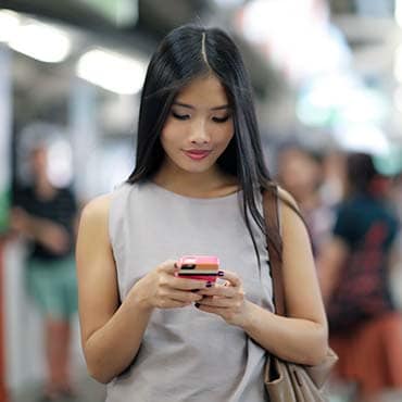 Asian woman looking at her phone while inside a subway station platform.