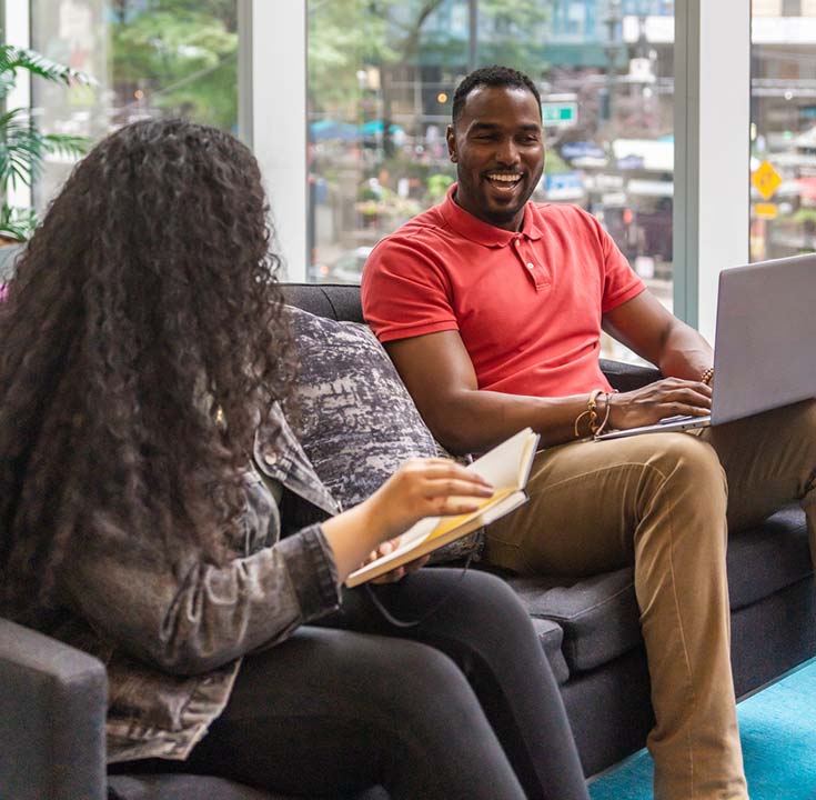 African American man with a laptop on his lap laughing with a woman