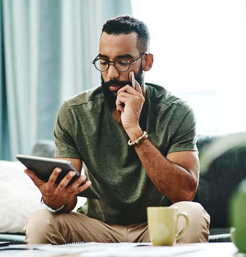 Man in green shirt and black glasses holding a pen and looking at his tablet