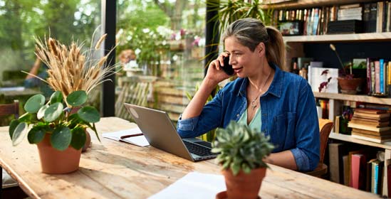 Businesswoman using mobile phone in front of laptop