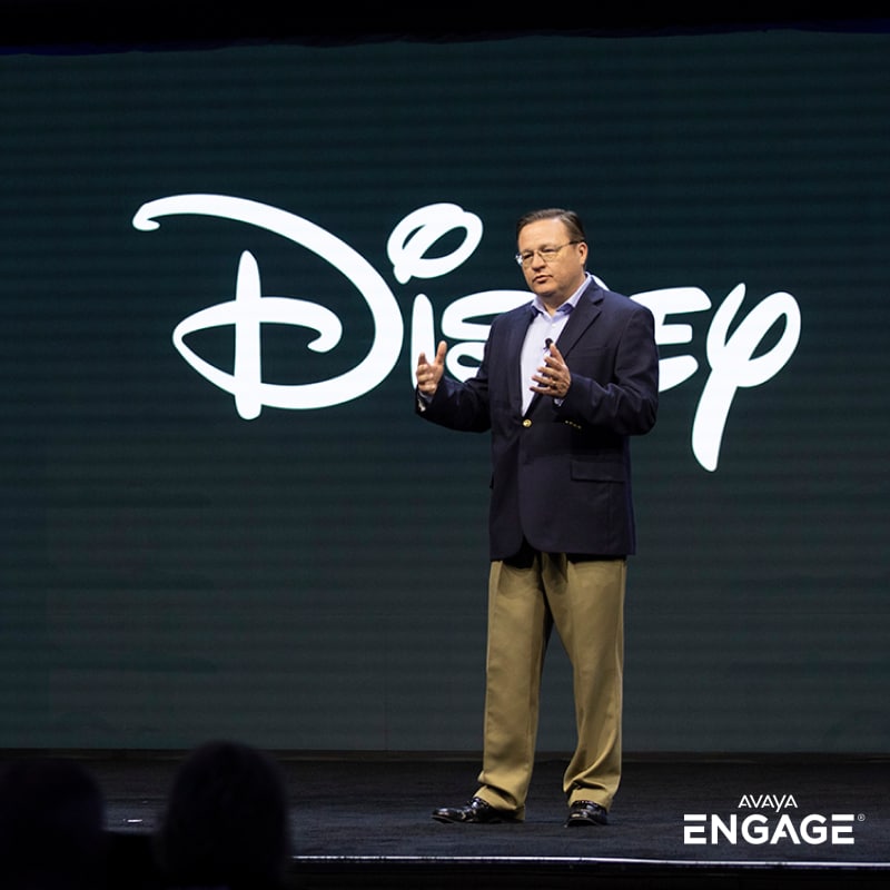 Un hombre disertando en un evento delante del logotipo de Disney